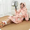 A woman is sitting on the floor, wearing a pink hoodie blanket with a rabbit pattern, and looking at her phone. Produktbild-Vorschau