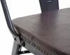 A close-up view of a brown faux leather seat with metal studs on a black metal chair frame. Produktbild-Vorschau