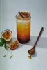 A glass of passion fruit juice with ice, garnished with a slice of passion fruit, and accompanied by passion fruit halves and a wooden spoon. Anteprima dell’immagine prodotto