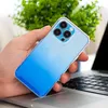 A hand holding a blue gradient phone case over a laptop keyboard, with a green plant in the background. Produktbild-Vorschau