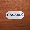 A close-up of a metal logo plate with the brand name 'CASARIA' on a wooden surface. Náhled obrázku produktu