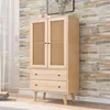 A wooden cabinet with cane doors and drawers, set against a stone-patterned wall. Produktbild-Vorschau