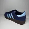 A side view of a navy blue Adidas Handball Spezial sneaker with light blue stripes and accents, set against a neutral background. Voir les images du produit