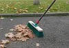 A broom is sweeping fallen leaves on a paved surface next to a grassy area. Anteprima dell’immagine prodotto