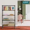 A black metal shelving unit with five shelves, filled with books, baskets, and decorative items, is placed in a room with green walls and a wooden floor. A dining table with chairs is visible in the background. Náhled obrázku produktu