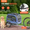 A dog sits next to a blue pet trailer attached to a bicycle, in an outdoor setting with trees and grass. Voir les images du produit