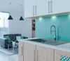 A modern kitchen and living area with a sink and faucet in the foreground and a sofa and pendant lights in the background. Produktbild-Vorschau