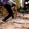 A person wearing work sneakers is breaking rocks with a sledgehammer near a rusty truck. Náhľad obrázku produktu