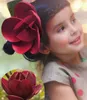 A young girl with a large red flower accessory in her hair, with a close-up of a red flower in the bottom left corner. Produktbild-Vorschau