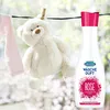 A teddy bear and a pink garment are hanging on a clothesline, with a bottle of laundry scent next to them. The background is blurred, suggesting an outdoor setting. Podgląd zdjęcia produktu