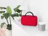 A red portable steamer sits on a white dresser next to a plant and a speaker. Produktbild-Vorschau