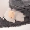 A close-up of a plush sheep toy lying on a gray blanket. Anteprima dell’immagine prodotto