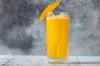 A glass of mango puree with a mango slice garnish on a wooden surface against a mottled gray background. Podgląd zdjęcia produktu