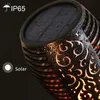 Close-up of a solar-powered garden light with a flame effect, showing water droplets on its surface. Produktbild-Vorschau