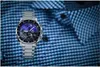A silver watch with a blue face is placed on a blue checkered shirt. Voir les images du produit