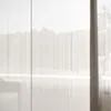 A white high-gloss wardrobe with a push-to-open mechanism, seen from the front with a slight diagonal angle, with sheer curtains in the background. Produktbild-Vorschau