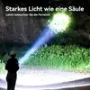 A person is shining a powerful flashlight into a dark, grassy area, illuminating the surroundings with a bright beam of light. Produktbild-Vorschau