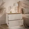 A white high-gloss nightstand with gold trim, featuring two drawers, a bust, and a decorative lamp. Produktbild-Vorschau