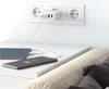 A white multi-port USB charger is plugged into a wall socket, charging a tablet and a smartphone on a nightstand next to a bed. Podgląd zdjęcia produktu