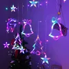 A string of colorful LED Christmas lights in various festive shapes like stars, bells, reindeer, and Christmas trees, hanging in front of a decorated Christmas tree. Produktbild-Vorschau