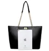 A black tote bag with gold chain straps is shown against a white background. An iPad is placed in front of the bag to show its size. Náhľad obrázku produktu