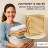 A woman is holding a laundry basket full of folded towels next to a wooden laundry hamper. Produktbild-Vorschau