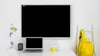 A desk setup with a large black screen, a laptop, a lamp, a camera, a glass of water, a lemon, and a yellow backpack on a ladder. Produktbild-Vorschau
