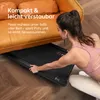 A woman is sliding a black walking pad under an orange couch. Produktbild-Vorschau