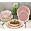 A set of pink and white reactive glaze dinnerware, including plates and bowls, arranged on a marble surface with a decorative plant in the background. Podgląd zdjęcia produktu