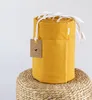 A rolled-up yellow fabric item with white ties, sitting on a woven stool. Produktbild-Vorschau