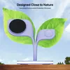 A purple charging stand designed to look like a plant with two leaves, set against a sky background and resting on a wooden surface. Podgląd zdjęcia produktu