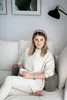 A woman sits on a couch holding a mug, leaning against a backrest pillow. Náhled obrázku produktu