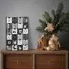 A black and white advent calendar with 24 drawers is placed on a wooden dresser, next to a vase with a Christmas tree branch and gingerbread decorations. Náhled obrázku produktu