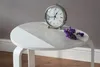 A close-up shot of a round table with a marble-like pattern and a white section, featuring a silver alarm clock and a small bunch of dried purple flowers. Podgląd zdjęcia produktu