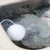 A white spherical device with a white cord is in a sink filled with soapy water and dishes. Podgląd zdjęcia produktu