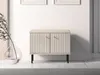 A beige cabinet with fluted doors and gold knobs, standing on black legs, is placed on a marble surface in front of a white wall. A glass vase with a plant is to the left. Náhľad obrázku produktu
