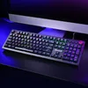 A black gaming keyboard with RGB backlighting is placed on a dark surface in front of a computer monitor. Produktbild-Vorschau