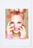 A woman with dramatic makeup and a bow-shaped hairstyle is posing with her hands near her face, showcasing her nails and accessories. Produktbild-Vorschau
