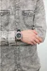 A person wearing a grey denim shirt and a Casio G-Shock watch on their left wrist. Anteprima dell’immagine prodotto