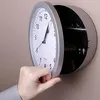 A hand is opening a wall clock that has a hidden compartment. Voir les images du produit