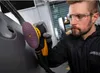 A man is using a sander on a car door in a workshop. Produktbild-Vorschau