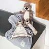 Three otter plush toys are arranged on a gray bench with a gray blanket. Náhľad obrázku produktu