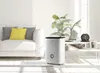A humidifier is placed in a living room next to a sofa and a coffee table with plants. Produktbild-Vorschau