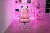 A pink gaming chair is set up in a room with pink ambient lighting, a desk with a laptop and computer monitor, and a shelf unit. Produktbild-Vorschau