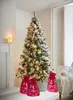 A decorated Christmas tree with three red gift bags in front of it, set in a cozy room with a fireplace and a window. Produktbild-Vorschau