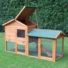 A wooden rabbit hutch with a green roof and wire mesh, set on a grassy lawn with a hedge in the background. Produktbild-Vorschau