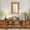 A well-lit interior scene featuring a wooden media console with various decorative items and books, a lamp, and a mirror on the wall. Podgląd zdjęcia produktu