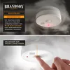 A split image showing a smoke detector on a ceiling with smoke, and a close-up of a finger pressing the test/deactivate button. Produktbild-Vorschau