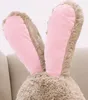 Close-up of a plush bunny's ears and head, resting on a light gray couch. Voir les images du produit
