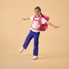 A young girl with a backpack is balancing on one leg against a plain background. Produktbild-Vorschau